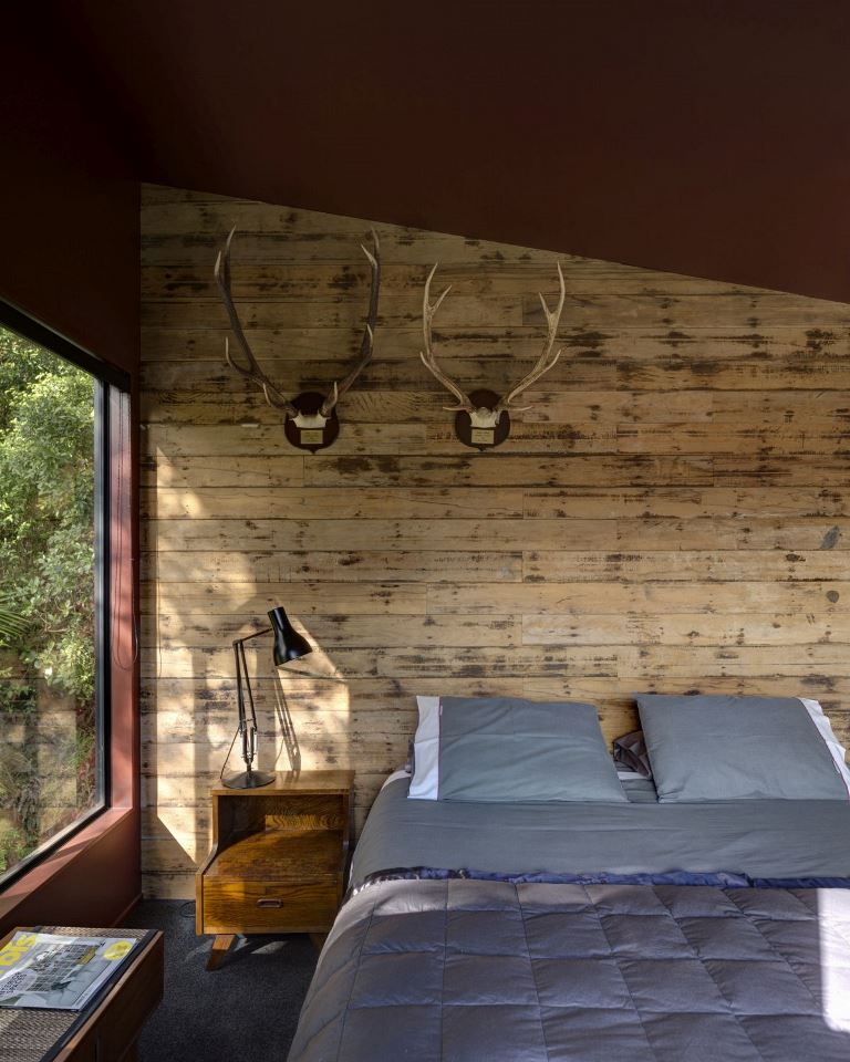 The bedroom is woodland-inspired, it features a wood paneled wall, antlers, some wooden furniture and a large bed
