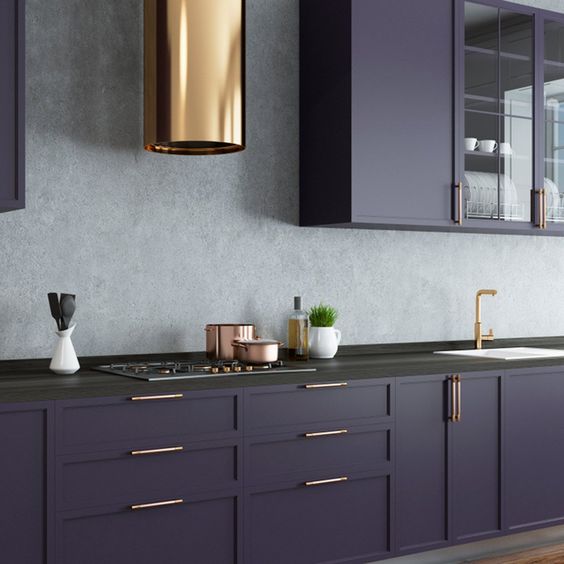 a dark purple kitchen with a grey stone backsplash, black stone countertops and touches of gold here and there