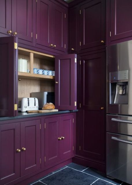 a moody vintage purple kitchen all clad with doors and panels and with gold knobs for an accent