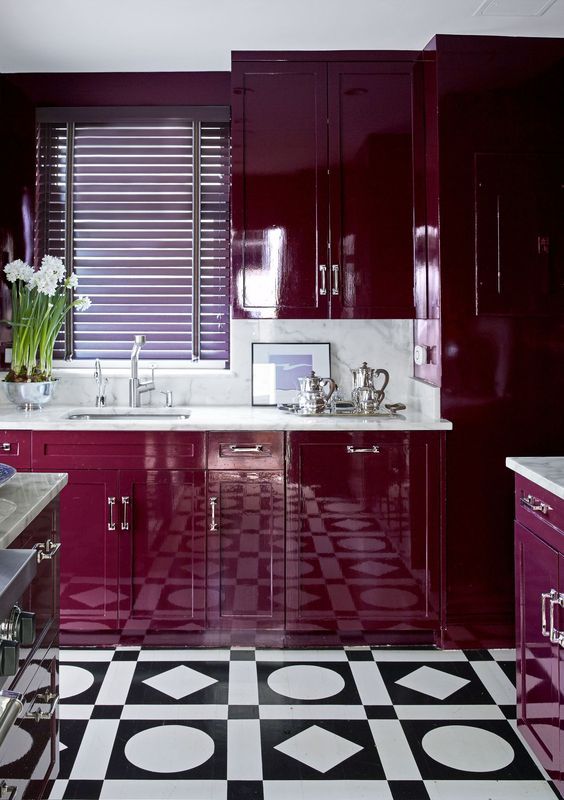 A super bold plum colored kitchen with white stone countertops and a backsplash and a mosaic tile floor is wow