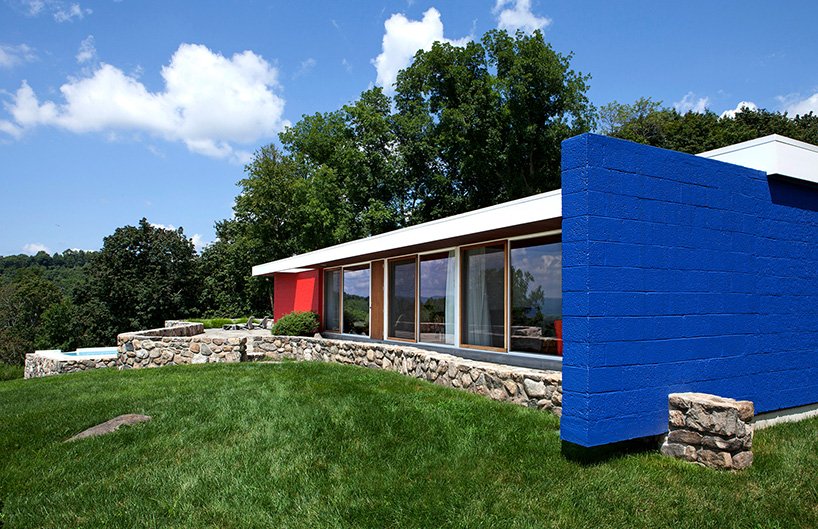 The house is done with red and blue touches and a mini fence is clad with stones, while the whole facade is glazed