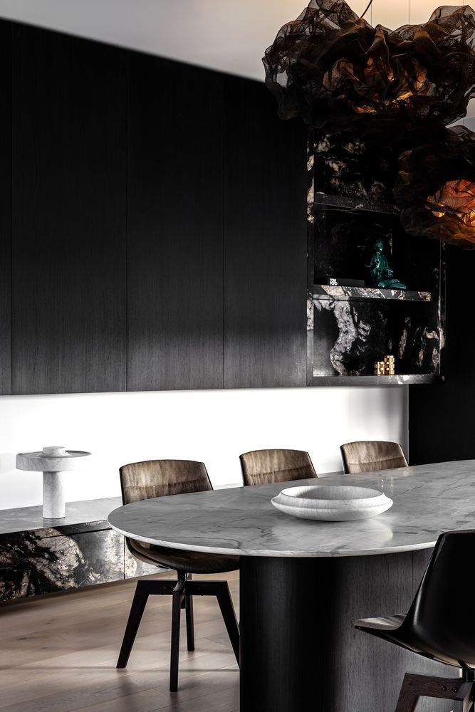 The dining room features black sleek cabinets, a marble top table, leather chairs and a black marble slab