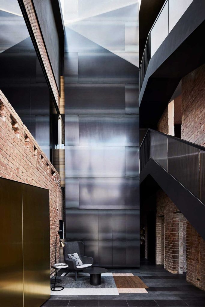 The entryway excites and astonishes with a polished metal wall, chic black furniture and brick walls