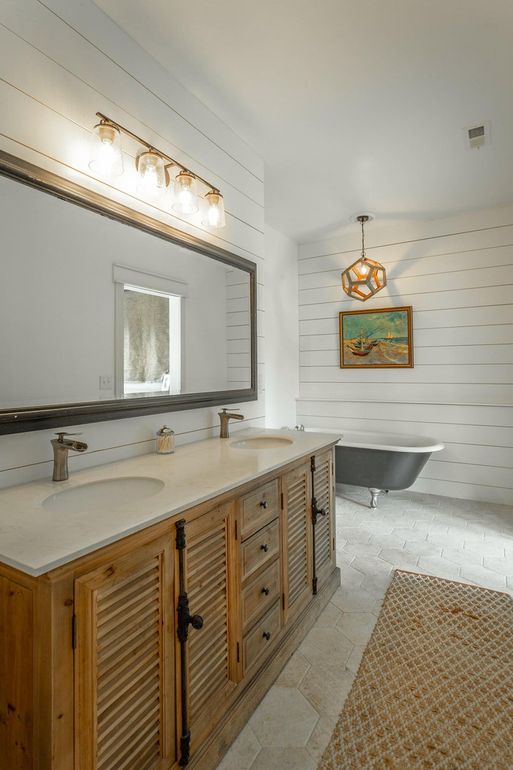 The master bathroom shows off hex tiles on the floor a wooden vanity, a rug and a black clawfoot tub