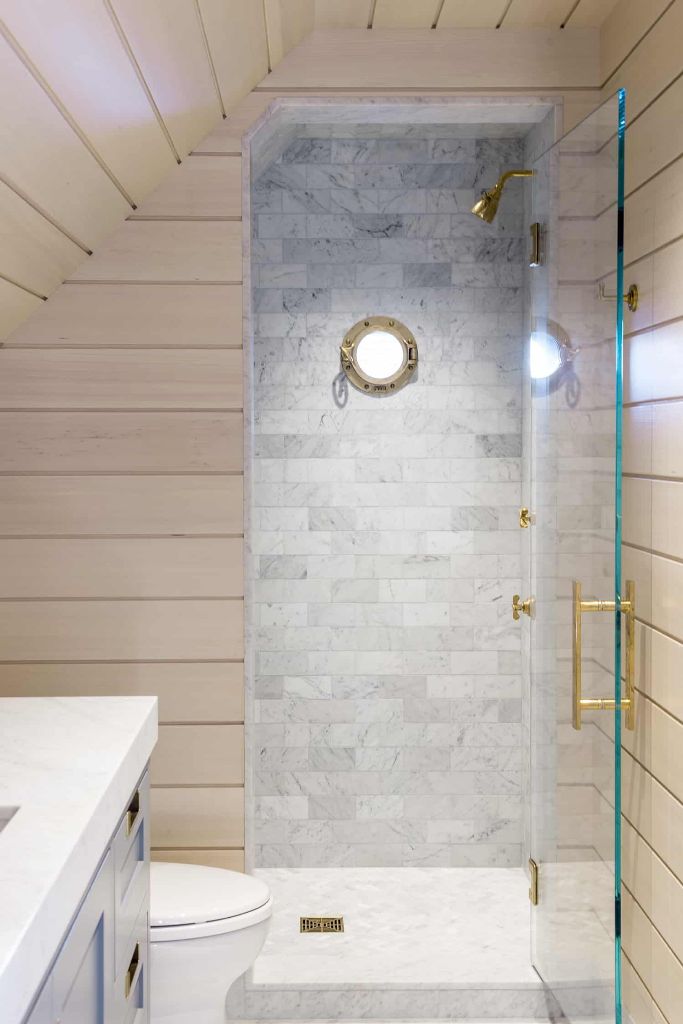 There's a small neutral bathroom with marble tiles and a porthole window to embrace the sea