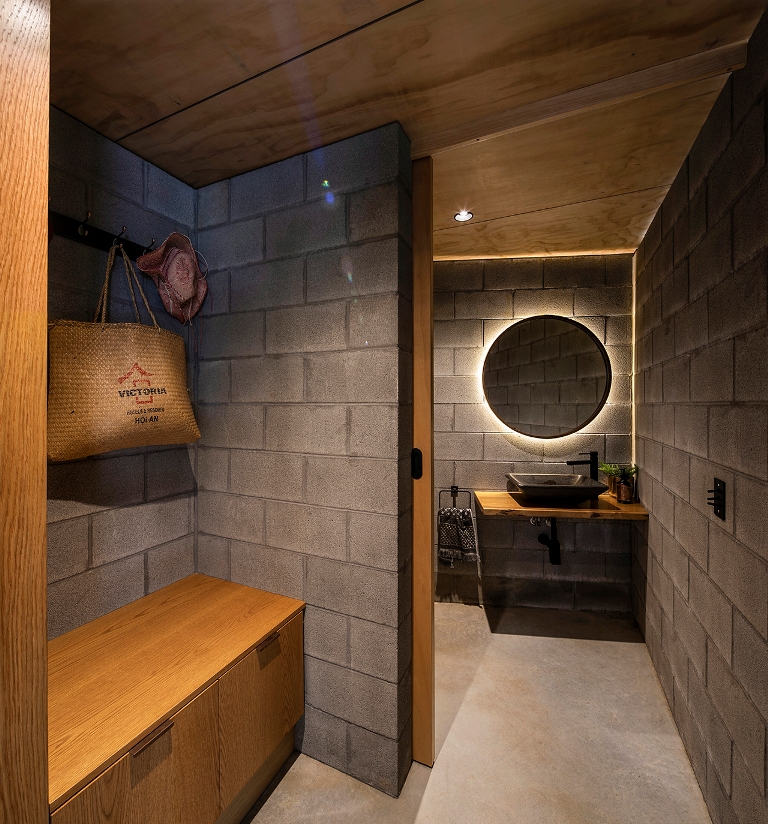 The bathroom continues the decor theme with concrete walls and floors, a lit up mirror and neutral stained wood