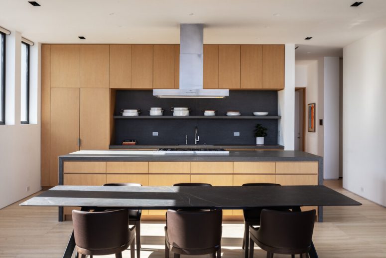 The kitchen is minimalist, with sleek neutral cabinets, a dark backsplash and there's a laconic dining space with a marble table