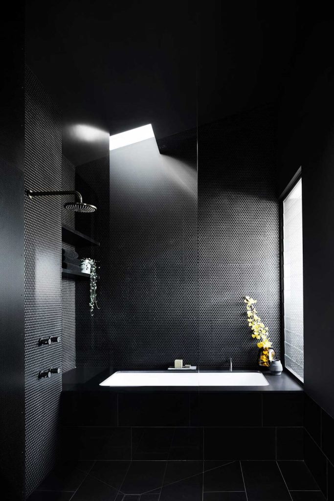 The black bathroom combines black penny and subway tiles and features windows