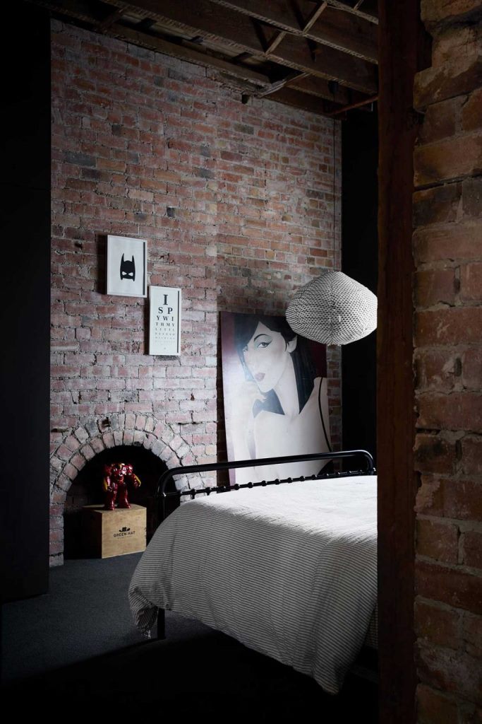 A guest bedroom shows off red brick, quirky artworks and a comfy metal bed