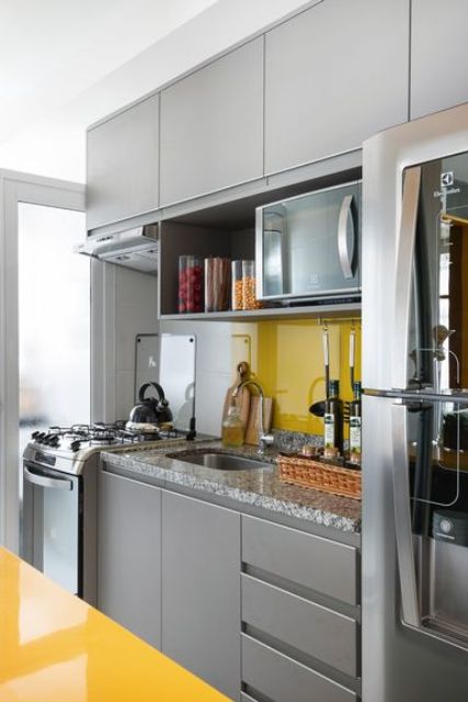 a bright minimal kitchen with sleek grey cabinetry, a bold yellow backsplash and a kitchen island to contrast