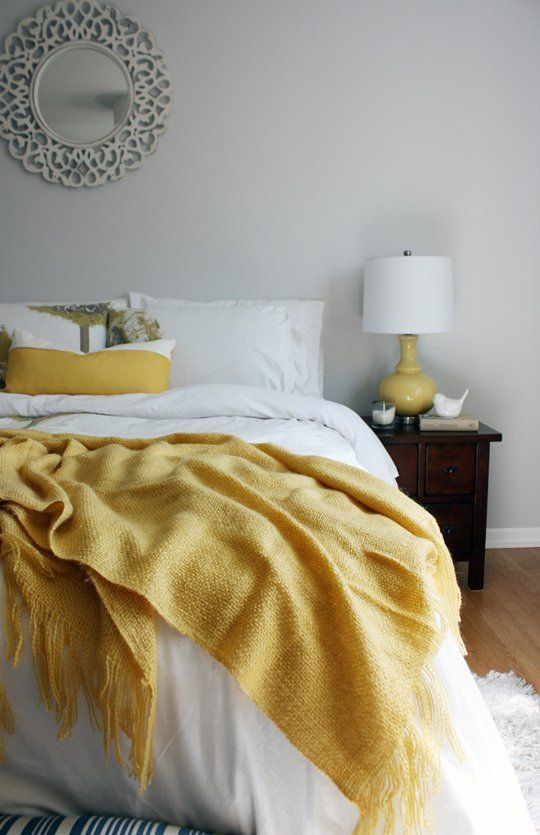 a chic bedroom with dove grey walls, white and sunny yellow linens, a mustard lamp and chic touches