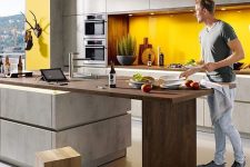a chic contemporary kitchen with matte grey cabinets, a sunny yellow backsplash and a kitchen island with a wooden tabletop