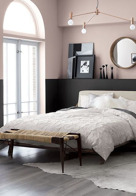 A chic modern bedroom with color block blush and black walls, a neutral bed, a mid century modern chandelier and a woven bench