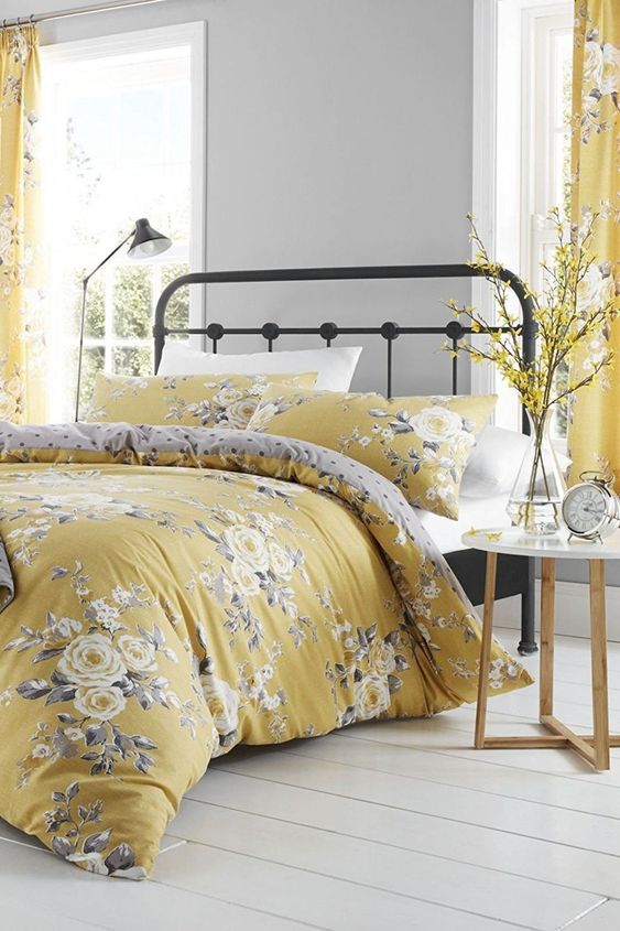 a chic romantic grey and yellow bedroom with dove grey walls, a metal bed, grey and yellow floral textiles and blooming branches