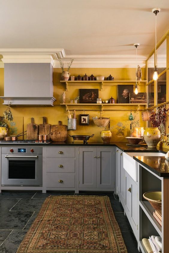a cozy eclectic kitchen with warm yellow walls and grey cabinets, black countertops and artworks on the shelves