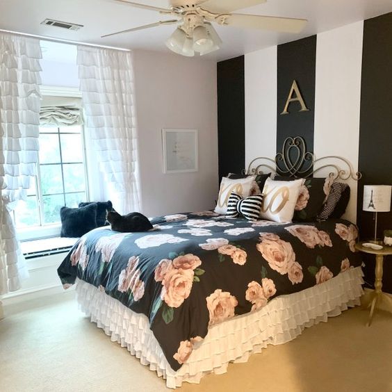 a glam and refined bedroom with a striped accent wall, black floral bedding, white ruffle curtains and exquisite furniture
