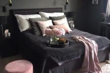a moody bedroom with grey walls, a black bed, nightstand and a pendant lamp, pink and black bedding and a pink ottoman