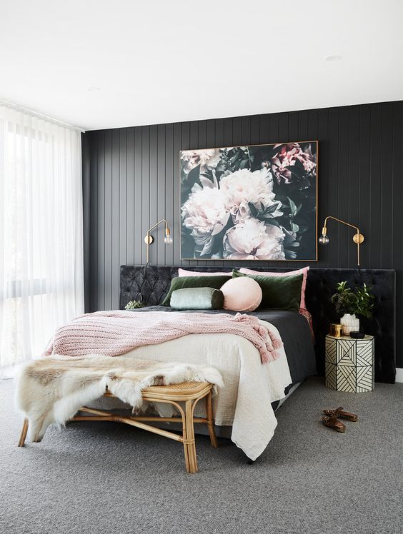 a refined bedroom with a black wooden accent wall, a black upholstered bed, pink and green bedding and a beautiful floral artwork