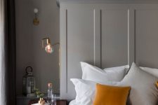 a refined bedroom with dove grey walls, molding, a vintage chest as a nightstand, mustard linens and touches of gold