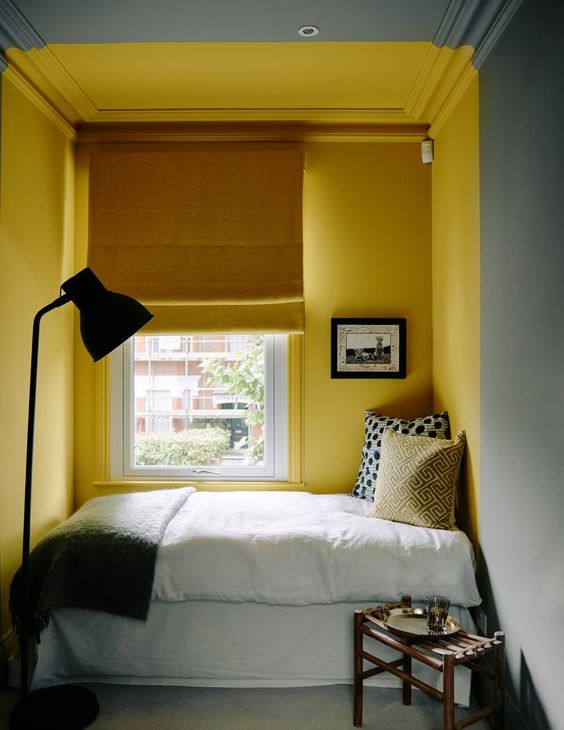 a small and cozy bedroom with grey walls and a sunshine yellow nook with a bed, a mustard curtain and grey and yellow bedding