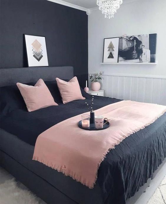 a small modern bedroom with a black statement wall, a black bed, pink and black bedding and a crystal chandelier
