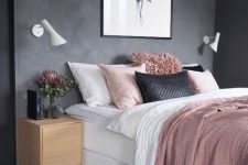 a stylish and simple bedroom with black walls, a white bed, pink and black bedding, floating nightstands and sconces