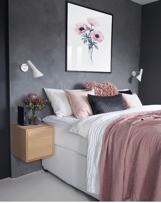 a stylish and simple bedroom with black walls, a white bed, pink and black bedding, floating nightstands and sconces