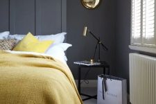 a stylish bedroom with graphite grey walls, simple and elegant furniture, lemon yellow textiles and gold touches