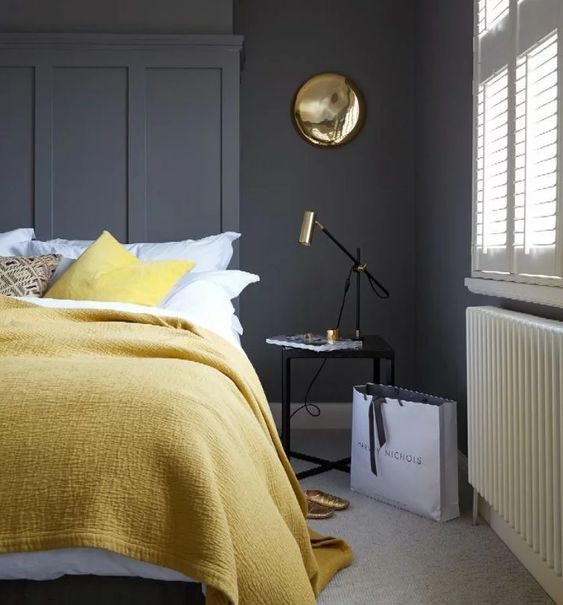 a stylish bedroom with graphite grey walls, simple and elegant furniture, lemon yellow textiles and gold touches