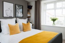a stylish contemporary bedroom with grey walls and a floor, a graphite grey bed, mustard linens and taupe curtains