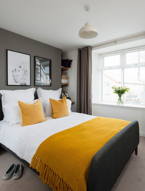 a stylish contemporary bedroom with grey walls and a floor, a graphite grey bed, mustard linens and taupe curtains
