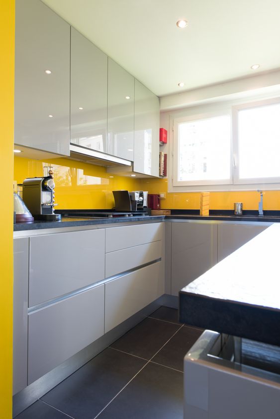 a stylish minimalist kitchen with white and dove grey cabinetry and a sunny yellow sleek glass backsplash stands out