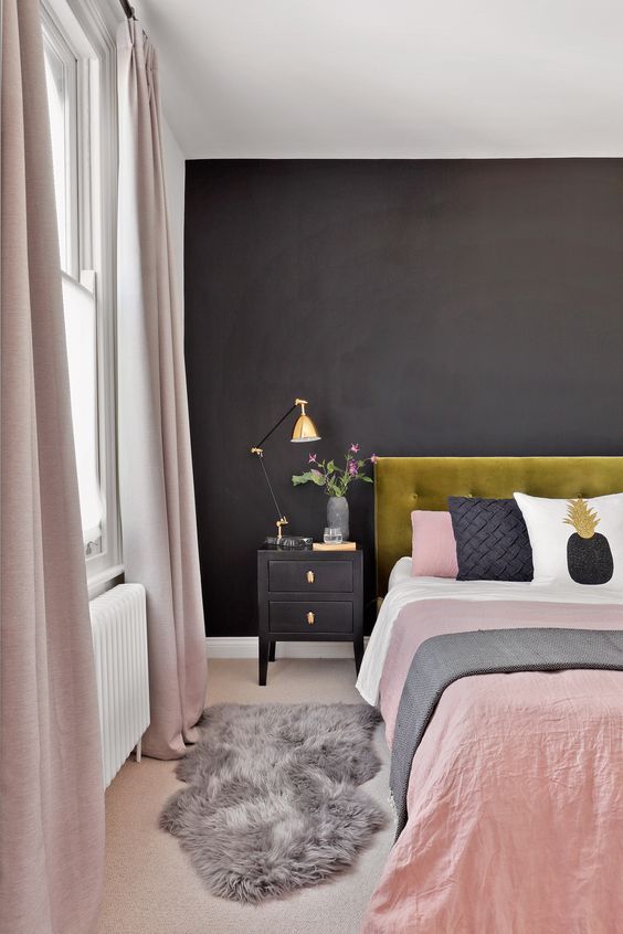a stylish modern bedroom with a black statement wall, a mustard velvet bed, black nightstands, blush linens and gold touches