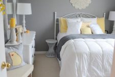 a traditional bedroom with grey walls, chic white furniture, grey and yellow bedding and touches of bright yellow