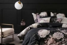 a very refined bedroom with black walls, paneling, black and pink floral bedding, a blush chair and a pendant lamp