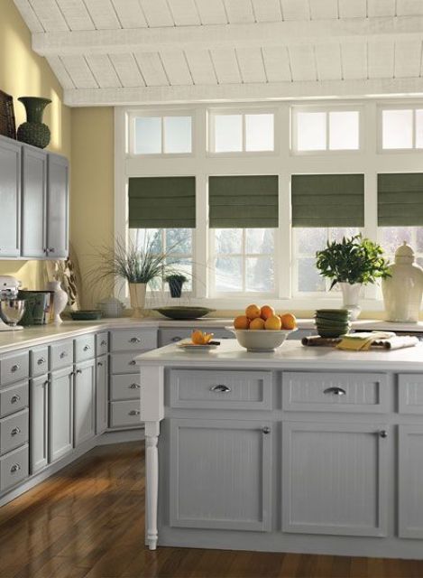 a welcoming farmhouse kitchen with pale yellow walls, stylish vintage-inspired cabinets in grey and green shades on the window