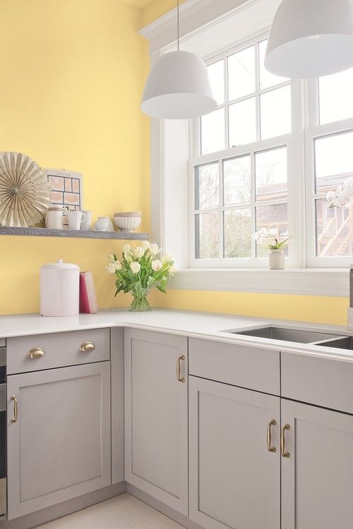 an airy kitchen with light yellow walls, dove grey cabinets and shelves, white pendant lamps and countertops