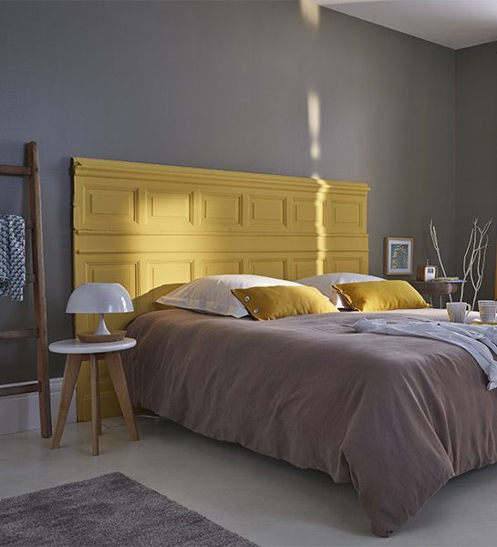 an eclectic bedroom with grey walls, a yellow paneled bed, grey and mustard bedding is very dreamy