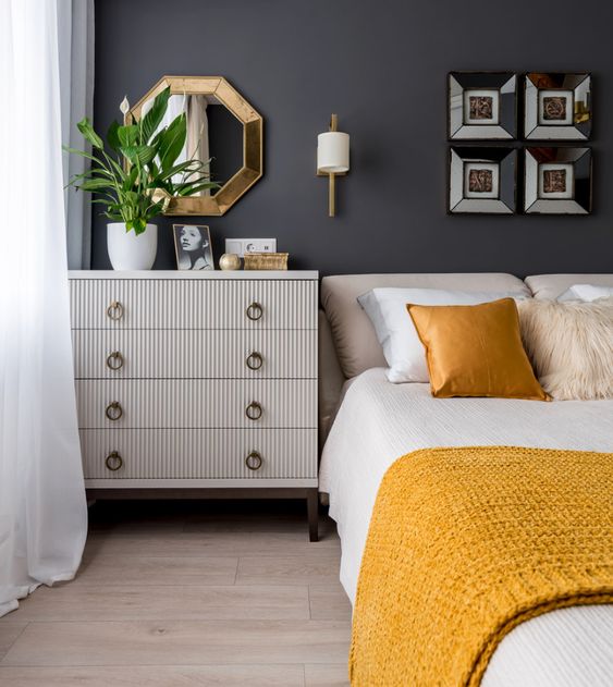An elegant mid century modern bedroom with graphite grey walls, neutral furniture, shiny and bright touches and yellow and white bedding