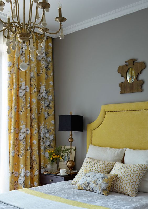 An elegant vintage inspired bedroom with light grey walls, a mustard bed, mustard floral curtains, a chic chandelier and grey and mustard bedding