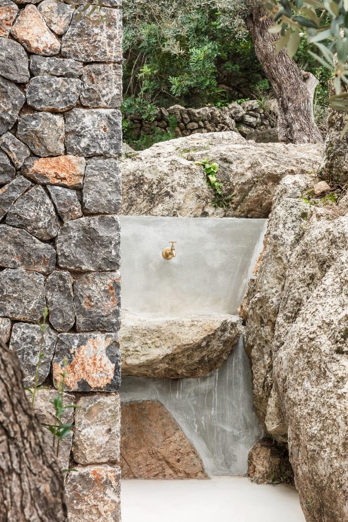 The sink is carved of stone outdoors and it features an elegant gold faucet