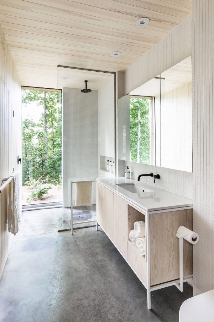 The bathroom is all-neutral, with white tiles and neutral plywood and a gorgeous forest view