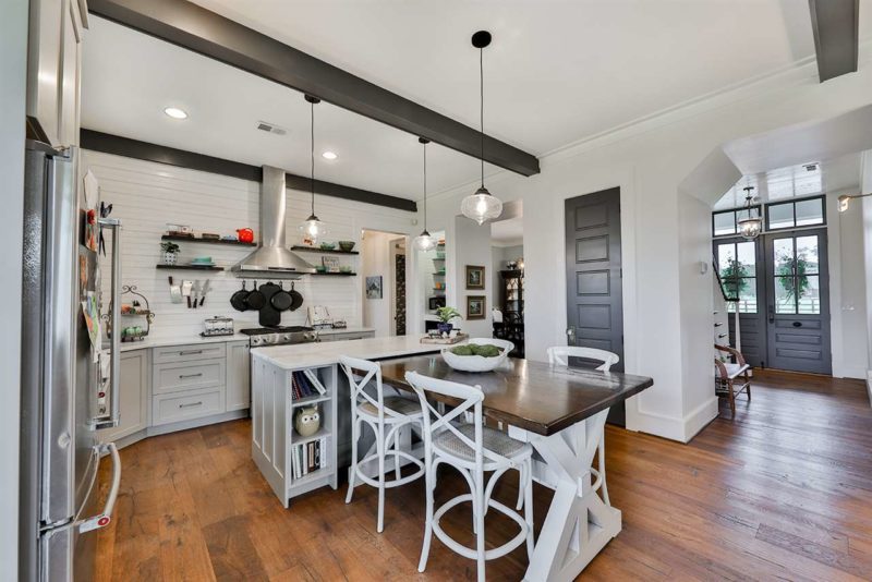 The kitchen is white, with a kitchen island and a trestle table that is attached to it for eating