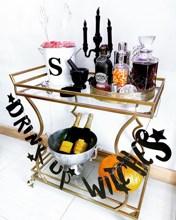 a Halloween drink station with a letter garland, a black candelabra with candles, skeleton hands and elegant drinks and candies