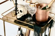a Halloween bar cart with skulls, a black candelabra with black candles, black cheesecloth, copper barware and elegant glasses