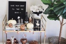 a Halloween bar cart with white and copper pumpkins, a sign, white blooms and skull drink stirrers