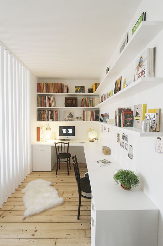 A Scandinavian home office with open shelves, an L shaped desk, black chairs, books, artwork, a rug and some lamps