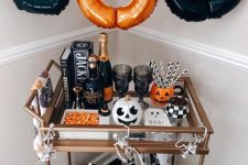 a bold Halloween bar cart with an orange and black letter garland, pumpkins, candies, an artwork and skeletons
