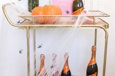 a bright Halloween bar cart with a pink sign, velvet pumpkins, bats on the wall, bright blooms and spiderwebs and spiders