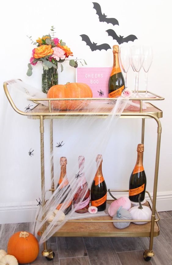 a bright Halloween bar cart with a pink sign, velvet pumpkins, bats on the wall, bright blooms and spiderwebs and spiders